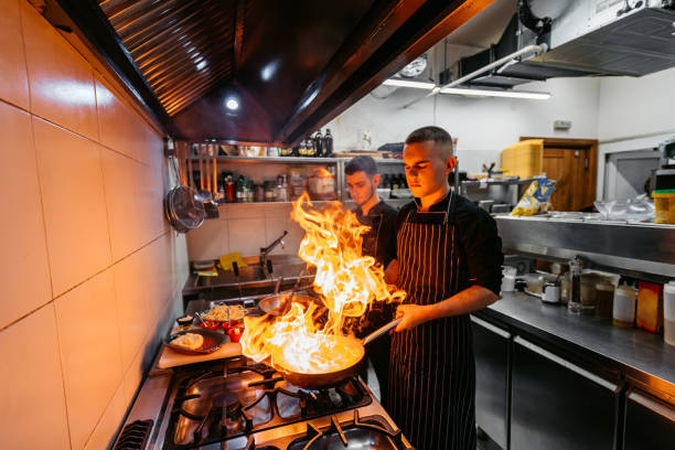 Chef And Sous-Chef Cooking With Fire In A Commercial Kitchen