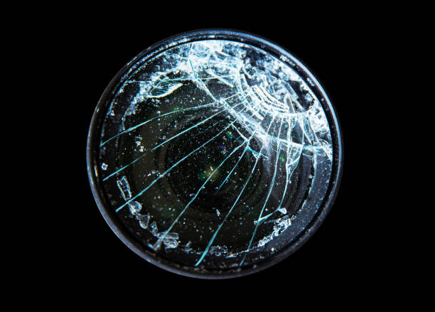 Closeup of a broken shattered camera lens with cracks, symbolizing damage and fragility of photography equipment, repair or replacement needs. Isolated on black background. Copy space
