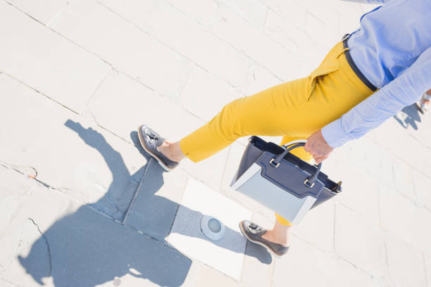 A person walking in bright yellow pants holding a stylish handbag. The photo captures a fashionable street style moment with a focus on the vibrant colors and accessories.