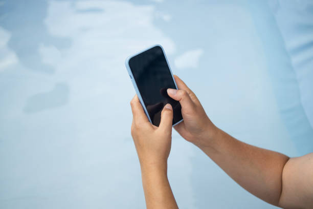 istock Young woman hand holding a black-screen cell phone outdoors on blue background 2182123800