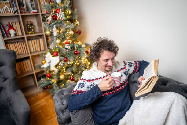 istock Man reading a book at home by the Christmas tree 2182127497