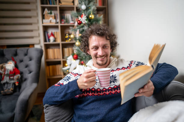 istock Man reading a book at home by the Christmas tree 2182128302