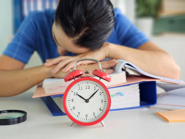 istock Tired office worker struggling to meet deadline and looking at alarm clock 2182129125