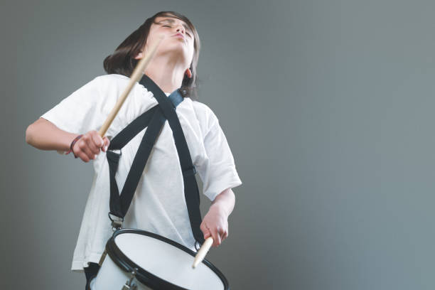 A young man plays the drum with drumsticks in his hands with great rhythm. The boy is wearing a white shirt and black tie