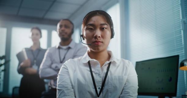 istock Serious Asian female hotline operator in headset looking at camera 2182135411