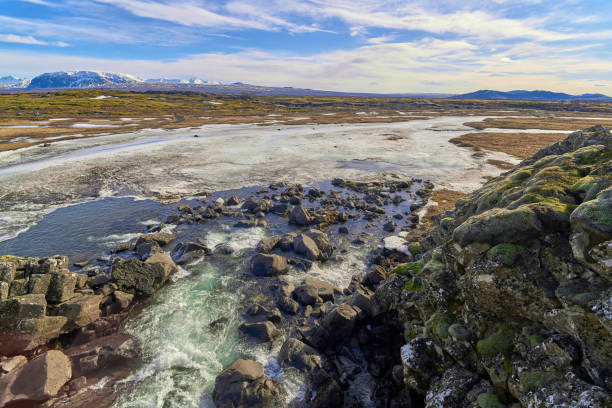 Water flowing over rocks in a river with snow and ice on the river banks in iceland