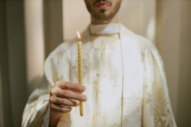 Medium close up of unrecognizable priests hand holding thin candle during church service