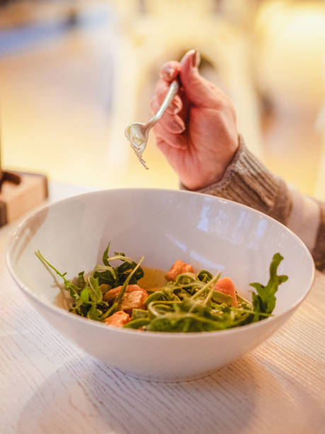 istock Eating in a restaurant: a hand with a fork above a white plate with green salad and salmon. 2182152136