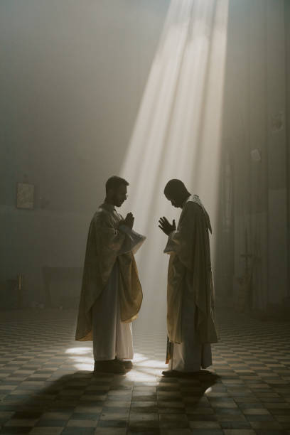 istock Men in Robes Praying Under Sunrays in Church 2182152215
