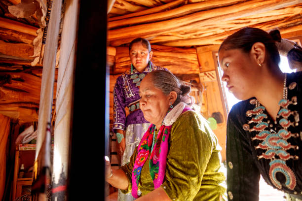 istock Traditional Elderly Navajo Woman Working to Make an Authentic Blanket on a Loom, Teaching Her Granddaughter and Spending Quality Time in a Traditional Navajo Hogan in Monument Valley Southern Utah, Northern Arizona 2182159364