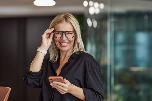 A cheerful and professional woman utilizing a smartphone in a stylish modern office setting