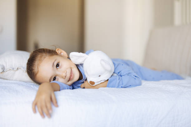 Two funny young children dressed in casual clothes playing and having fun on white bed. Studio shooting on white background