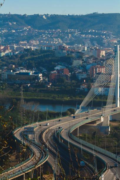 istock a winding, modern bridge with multiple lanes, curving gracefully as it leads into the urban landscape of Coimbra. The bridge is designed with a sleek architectural style, and its cables are visible as they support the structure. 2182177404