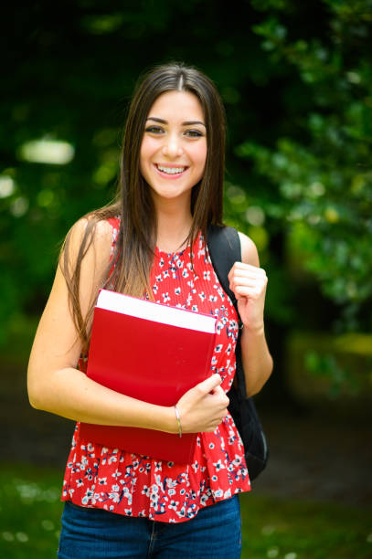 istock Smiling student holding books and wearing backpack in park 2182185950