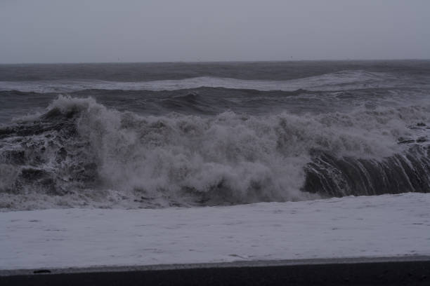 Giant ocean waves crashing on a black sand beach during a storm with white sea foam
