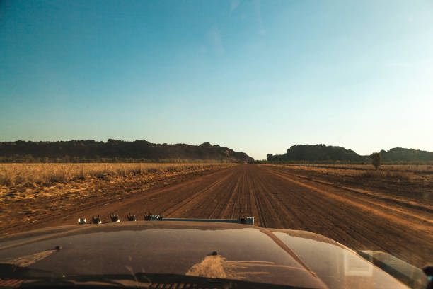 Driving along Gibb River Road reveals the vast and remote landscapes of Western Australia, with dry earth underfoot and rugged hills on the horizon during a clear afternoon.