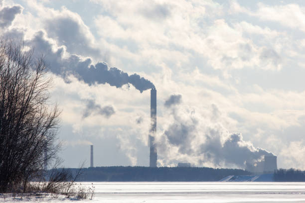 A large industrial plant is emitting smoke into the sky. The sky is cloudy and the sun is barely visible. Concept of pollution and industrialization