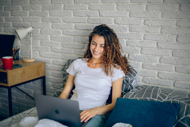 istock Smiling woman using laptop while relaxing on bed in the morning 2182222908