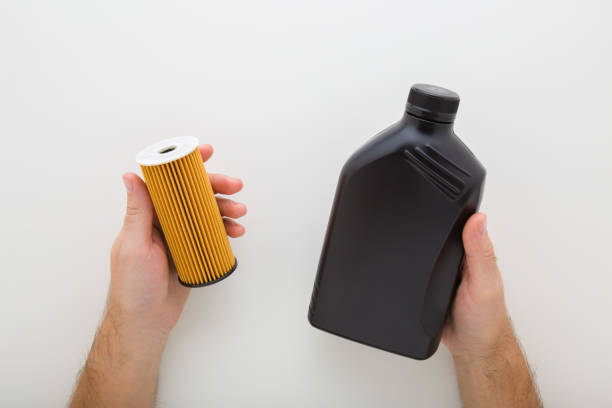 Young man hands holding and showing car new oil filter and dark black plastic container for car motor on light gray background. Closeup. Point of view shot. Top down view.