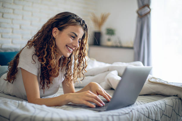 istock Smiling woman using laptop while relaxing on bed in the morning 2182223301