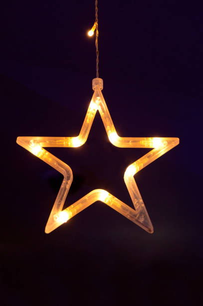 Vertical shot of one star shape outlined, glowing illuminated string soothing soft yellow light for Christmas festive celebrations, Diwali, New Year's reception party backdrops, greeting cards, wallpaper. There is blank copy space.