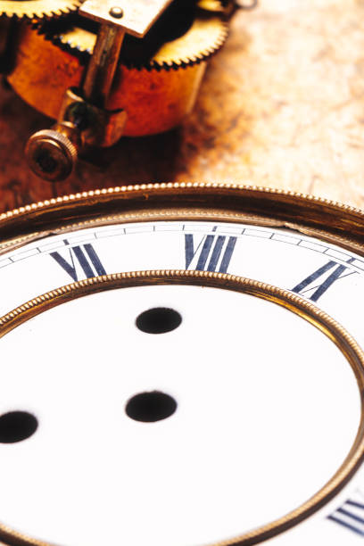 Antique clock dial with Roman numerals and gold-edged frame sits on a workbench. Visible apertures for hands and nearby gears suggest ongoing restoration of this delicate timepiece