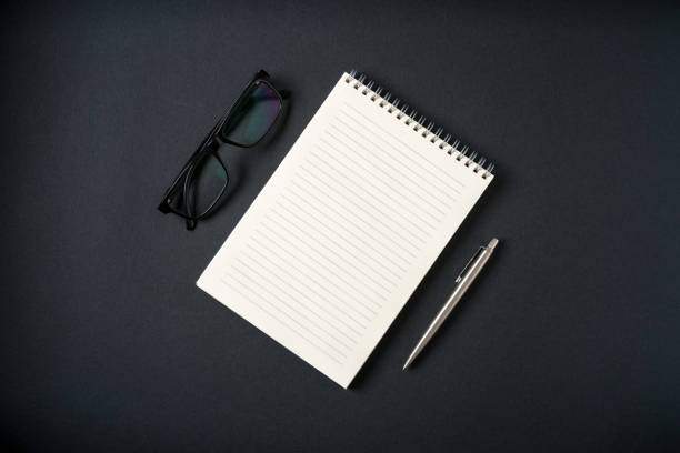 istock Top view of notebook, glasses and ballpoint pen on dark grey background 2182235401