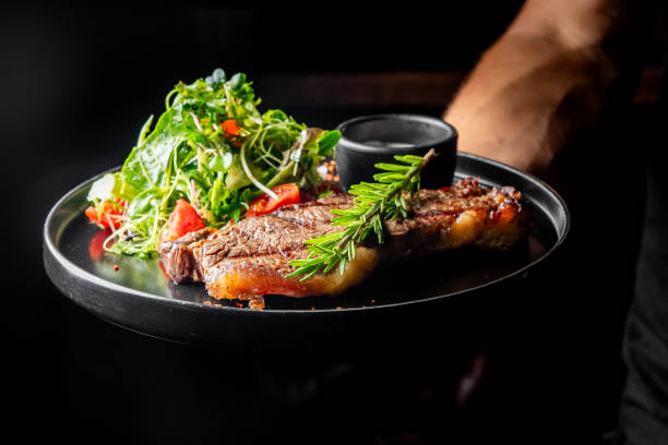 istock gourmet dish featuring perfectly grilled steak, accompanied by a fresh salad and a side of sauce, elegantly presented on dark plate. Ideal for culinary, food photography, and restaurant menu concepts. 2182241817