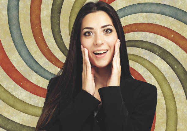 Close-up of a woman with wide eyes and a surprised expression. She wears a pink sweater and her hair is pulled back.