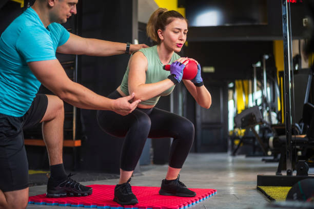 istock Personal trainer helping woman doing squats with kettlebell in gym 2182243558