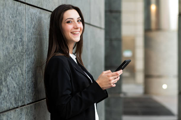istock Smiling businesswoman using smartphone leaning against wall 2182244594