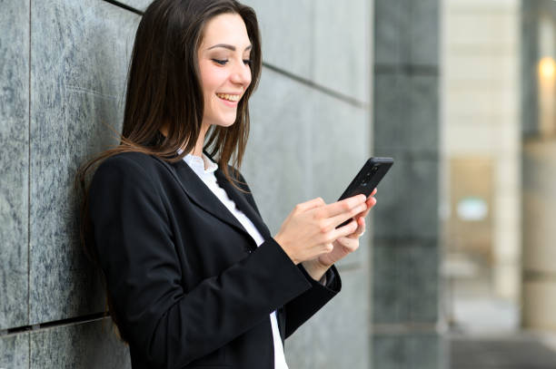 istock Smiling businesswoman leaning against wall using smartphone 2182244825