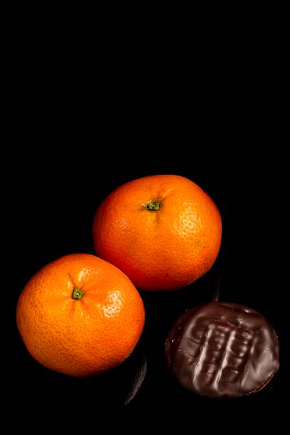 Chocolate biscuit, filled with orange, strawberry, peach and lemon jam, accompanied by orange fruit and on a black background. Vertical photo and selective focus