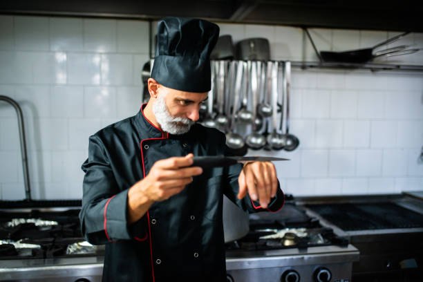 istock Professional chef sharpening knife and checking time in restaurant kitchen 2182246343