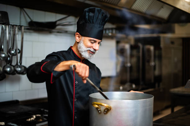 istock Mature chef mixing ingredients in a large pot, smiling, in a commercial kitchen 2182246511