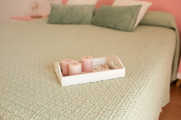 Home aroma fragrance diffuser with burning candles on white tray in bed over glowing lights close up. Cozy atmosphere. Wellness. Healthy lifestyle.