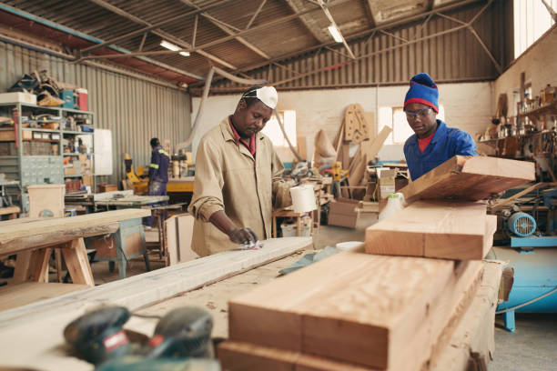 istock Two carpenter shop workers stacking planks and painting them with varnish 2182262308