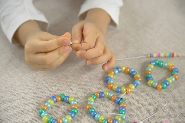 Close-up of a child's hands threading colorful beads onto a string, concentrating on creating a handmade bracelet. This image captures creativity, fine motor skills, and playful learning.