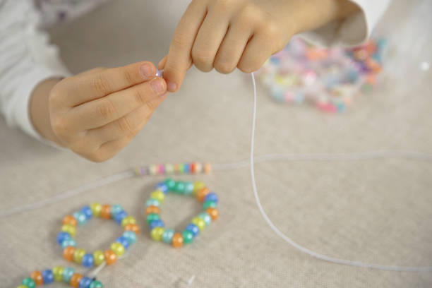 istock Close-up of a child's hands threading colorful beads onto a string, concentrating on creating a handmade bracelet. This image captures creativity, fine motor skills, and playful learning. 2182275743