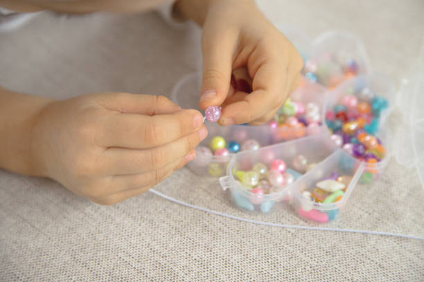 Close-up of a child's hands threading colorful beads onto a string, concentrating on creating a handmade bracelet. This image captures creativity, fine motor skills, and playful learning.