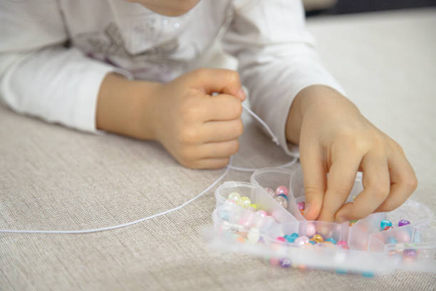 istock A young child carefully selects beads from a container to thread onto a string, demonstrating focus and creativity in making a colorful DIY jewelry piece. 2182275752