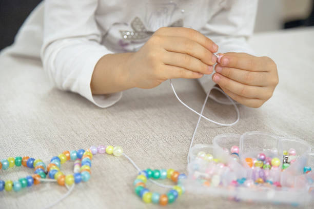 istock Close-up of a child's hands threading colorful beads onto a string, concentrating on creating a handmade bracelet. This image captures creativity, fine motor skills, and playful learning. 2182275762