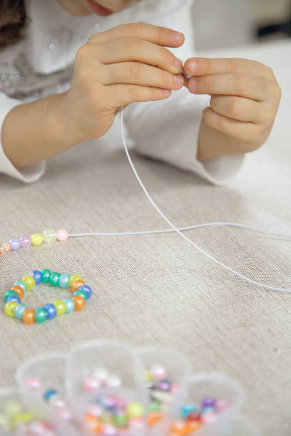 istock Close-up of a child's hands threading colorful beads onto a string, concentrating on creating a handmade bracelet. This image captures creativity, fine motor skills, and playful learning. 2182275778