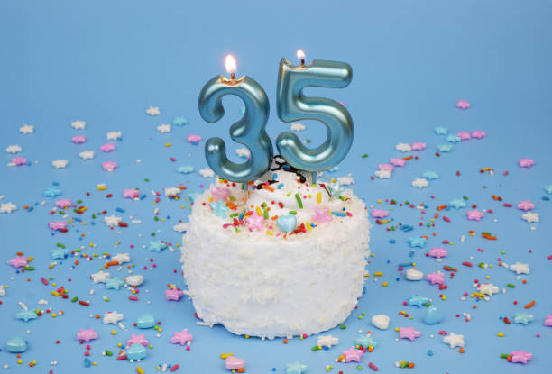 istock Coconut birthday cake on blue background with burning candle, number 35 2182286518