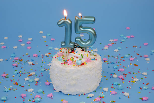 istock Coconut birthday cake on blue background with burning candle, number 15 2182286523