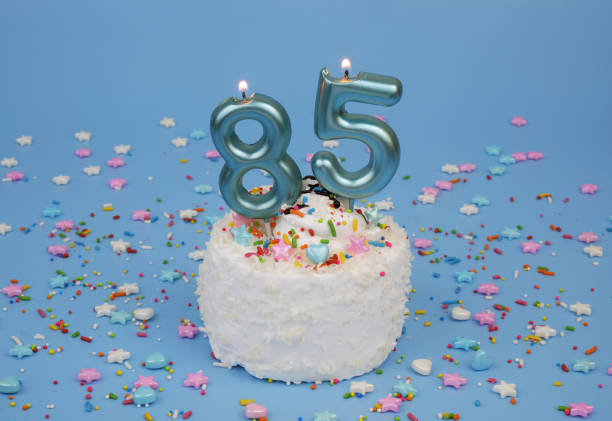 istock Coconut birthday cake on blue background with burning candle, number 85 2182286572