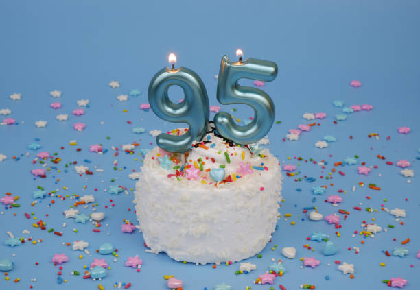istock Coconut birthday cake on blue background with burning candle, number 95 2182286582