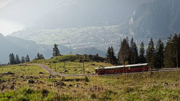 istock Red train journey through lush green mountains. 2182291136