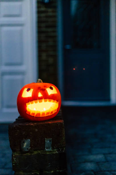 A Jack O' Lantern, illuminated by candles, sits on a wall outside a residential house on Halloween.