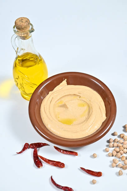A bowl of hummus, small jar, and chili peppers on a table